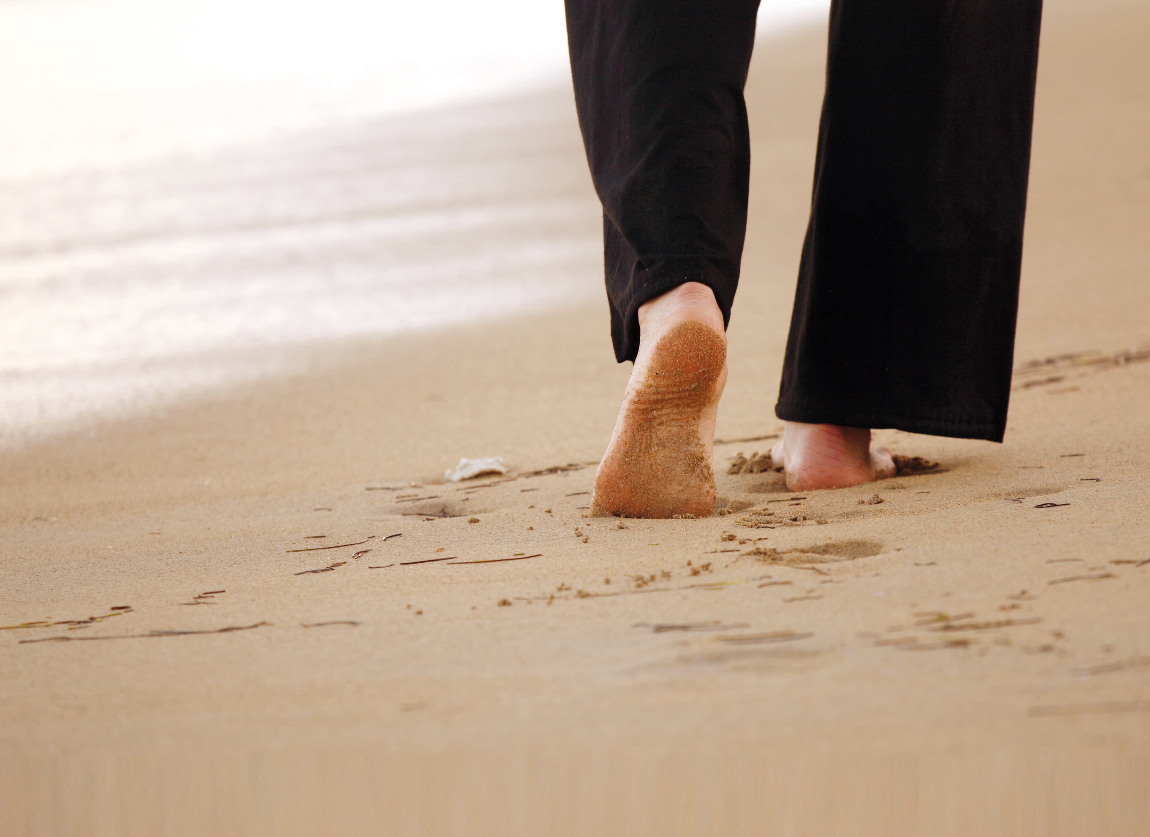 Bild von einer Person, die barfuß am Strand läuft.